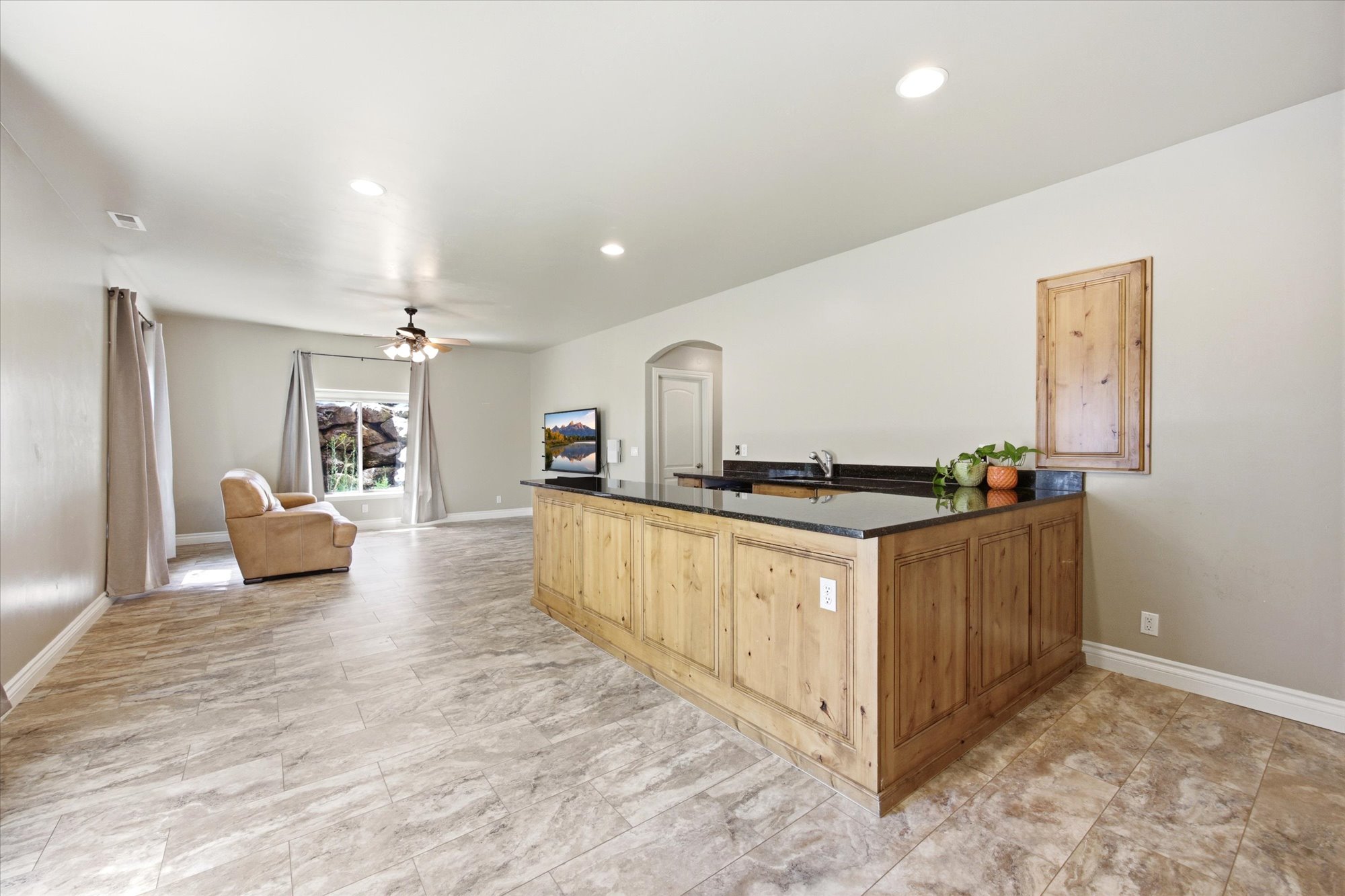 Spacious open-concept room featuring light wood-finish cabinetry with a black countertop and an integrated sink