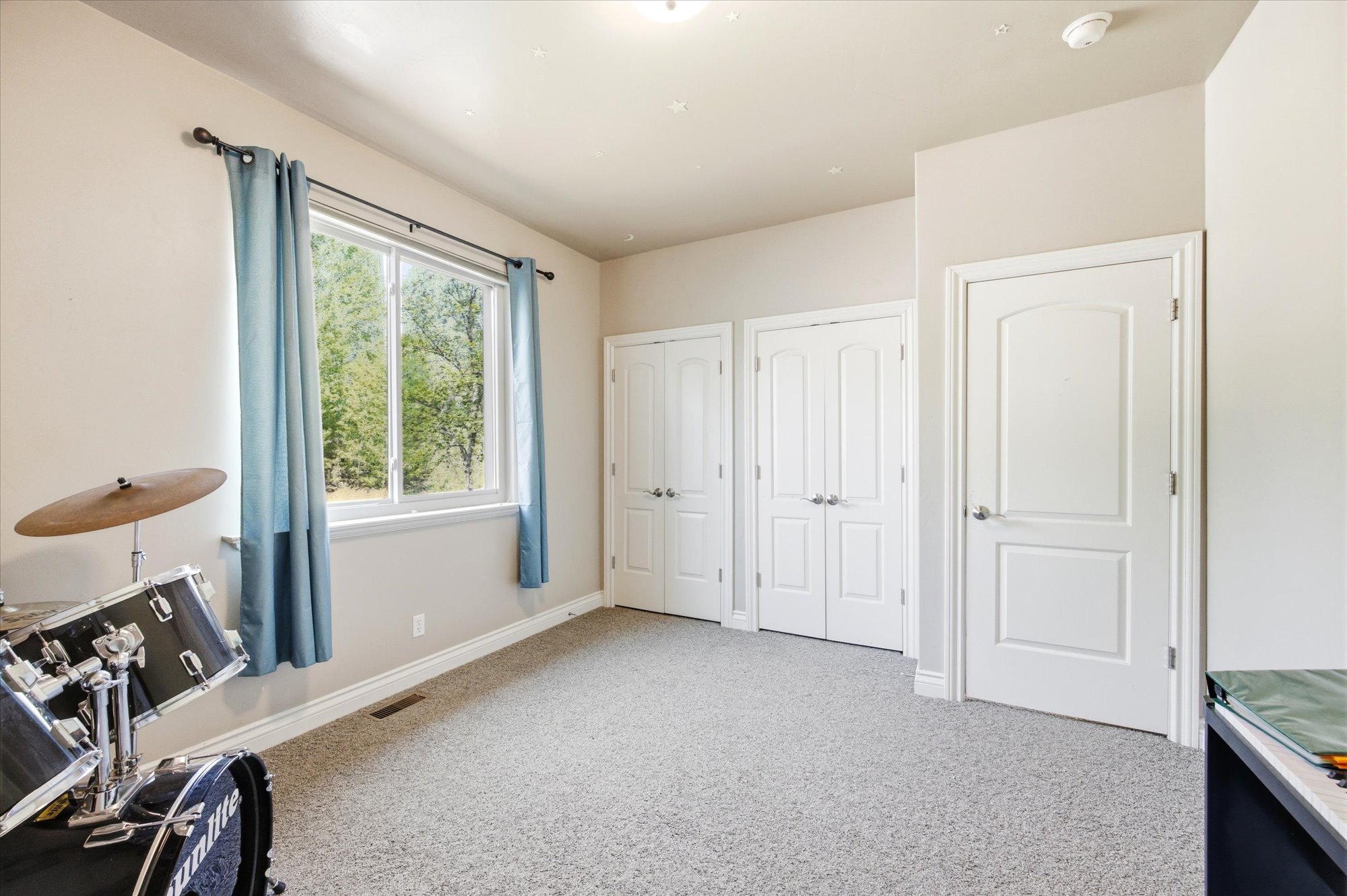 Carpeted room featuring a large window with blue curtains, two bifold closet doors, and a single paneled door