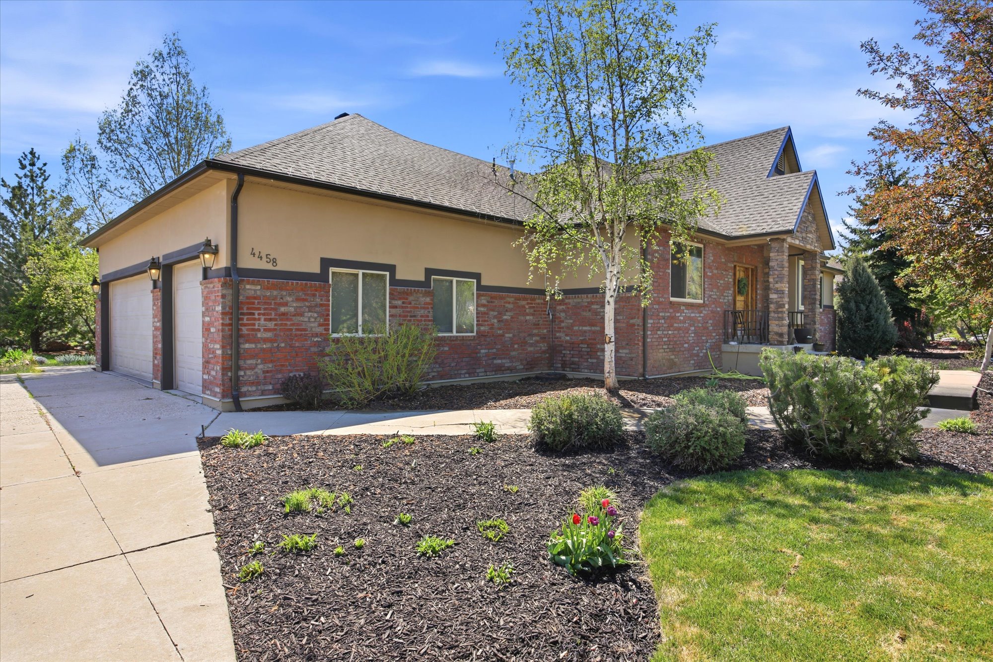 Brick and stucco exterior featuring a dual-bay garage with individual doors, a covered front entry, and mature landscaping