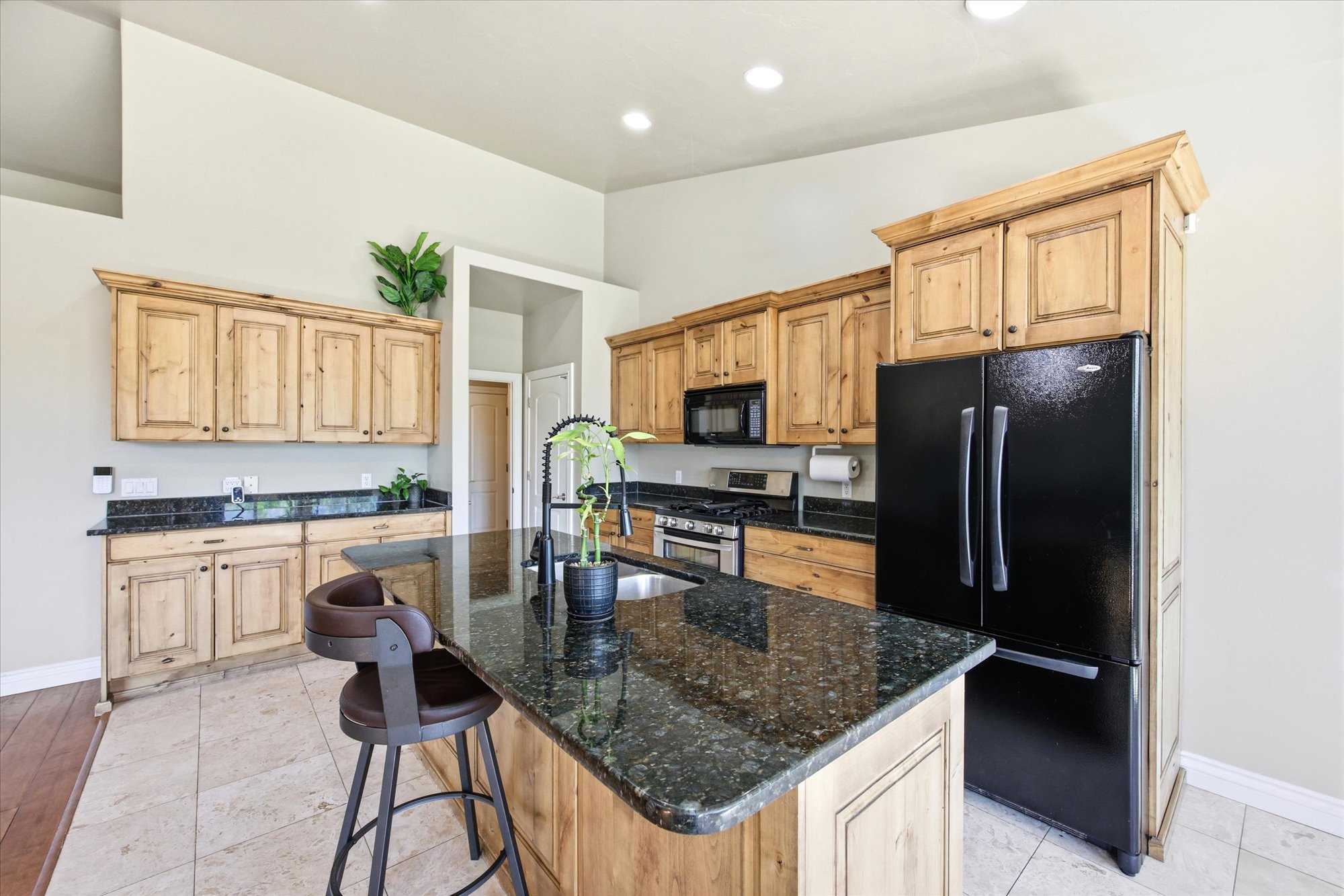 Spacious kitchen featuring an island with a dark granite countertop, light wood cabinetry, and a black appliance suite