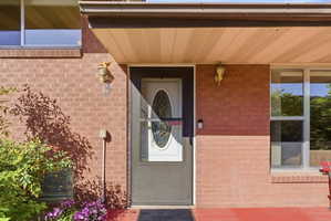 Brick exterior featuring a storm door with an oval glass insert, an overhead light fixture, and a built-in planter with foliage