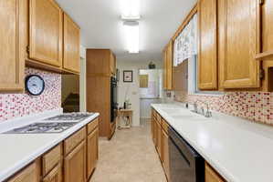 Galley kitchen featuring wood cabinetry, white countertops, tile flooring, a mosaic tile backsplash, and a double basin sink