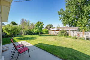 Expansive backyard featuring a concrete patio, a manicured lawn, and mature trees, all enclosed by a wooden fence