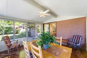 Sunroom featuring a ceiling fan, brick wall, wood-finish flooring, and expansive windows overlooking the backyard