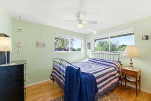 Bedroom featuring light green walls, wood-finish flooring, and a ceiling fan with integrated lighting