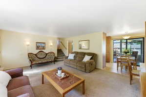 Spacious living area featuring neutral carpeting, a staircase with neutral carpeting, and wall sconces