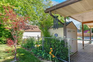 Covered patio space featuring a chain-link fence, mature trees, and a detached storage shed