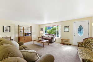 Spacious living area featuring neutral carpeting, a prominent front entry door with an oval glass insert, and a large picture window providing exterior views
