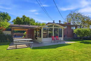 Expansive backyard featuring a lush lawn, sunroom with large windows, covered patio area, and mature trees