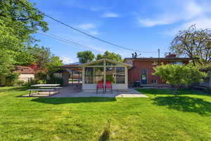 Expansive backyard featuring a manicured lawn, a sunroom with large windows, and a concrete patio