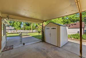 Covered concrete patio with chain-link fencing and a separate storage shed