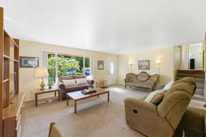 Living room featuring large picture windows, light-toned carpeting, a white entry door with an oval glass insert, and built-in shelving