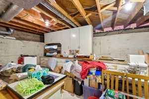 Unfinished basement space featuring exposed wooden ceiling joists, concrete foundation walls, and built-in white cabinetry with a countertop