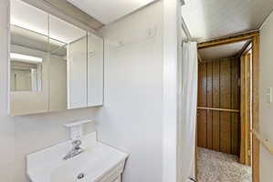 Bathroom featuring a white vanity with integrated sink, two mirrored medicine cabinets, wall-mounted light fixtures, and a shower area with a curtain rod