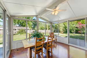 Sunroom featuring numerous windows, glass sliding doors, a ceiling fan with integrated lighting, and high-gloss flooring