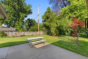 Expansive backyard featuring a concrete patio, a manicured lawn, and mature trees providing natural screening