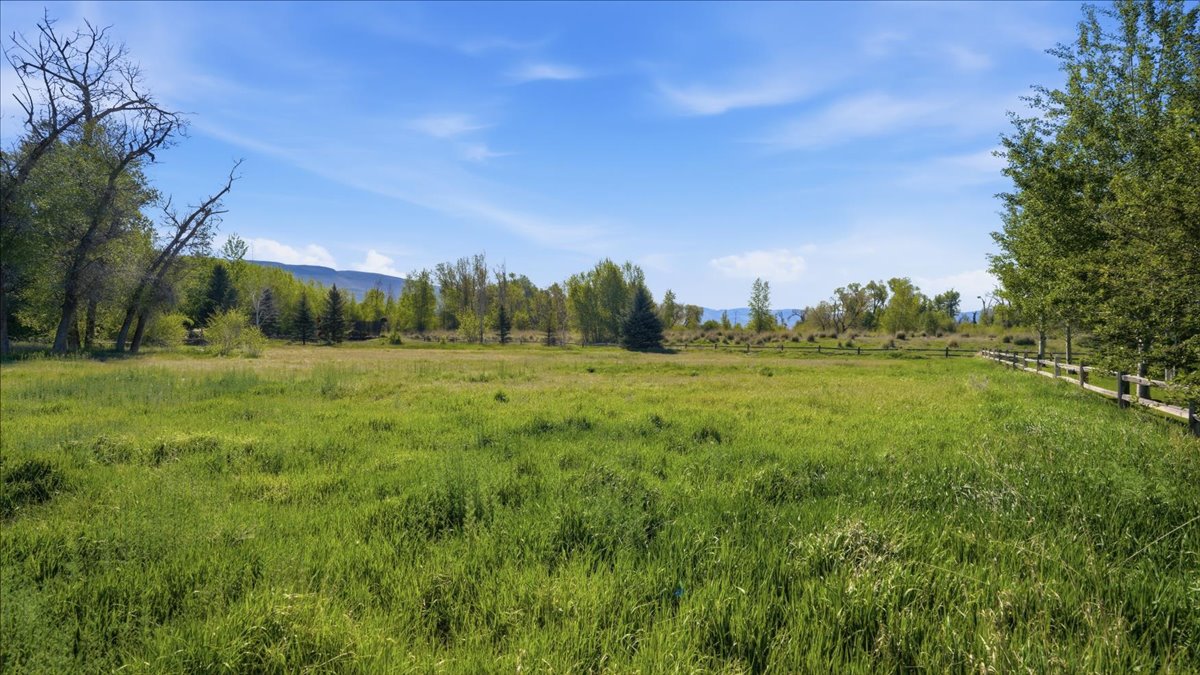 Expansive green field with natural grass and a split-rail fence border