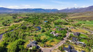 Expansive rural landscape featuring a winding river, mature trees, open fields, and distant snow-capped mountains under a clear sky