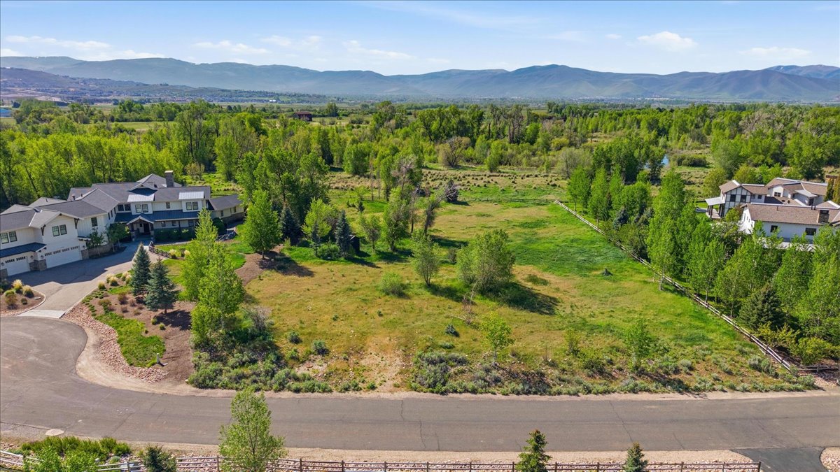 Expansive land parcel featuring open green space, mature trees, mountain backdrop, and paved road frontage