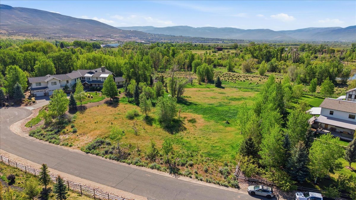 Expansive property featuring a large residence, a paved circular driveway, mature trees, open green spaces, and mountain scenery