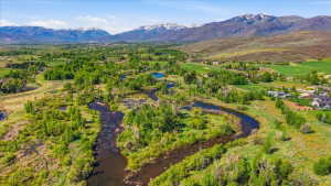 Expansive natural landscape featuring a winding river, lush green foliage, distant snow-capped mountains, and scattered residential properties