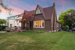 Tudor Revival architecture featuring a prominent brick exterior, a bay window with multiple panes, a steeply pitched roof with dark shingles, and a substantial brick chimney