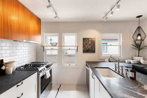 Contemporary kitchen featuring white shaker cabinetry, dark countertops, a subway tile backsplash, and stainless steel appliances