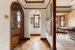 Entryway featuring a rich wood-finish arched door with a narrow window, geometric wood-finish flooring, and crown molding
