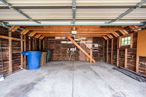 Spacious garage featuring a concrete floor, exposed wood beam ceiling, exposed wood plank walls, and a multi-pane window