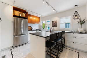 Modern kitchen featuring a central island with countertop seating, white cabinetry, dark stone countertops, and a white subway tile backsplash