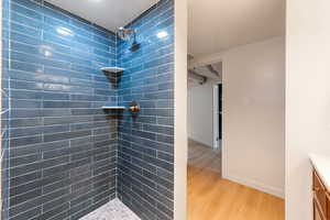 Walk-in shower featuring blue subway tile walls, a rain showerhead, brushed brass fixtures, and a pebble tile floor