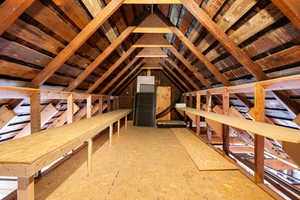 Garage storage space featuring exposed wooden beams, unfinished wood flooring, and built-in wooden shelving along both sides