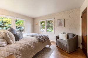 Bedroom featuring multiple windows, wood-finish flooring, a wall-mounted sconce, a paneled wood door, and textured wall coverings