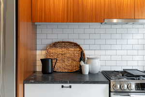 Contemporary kitchen featuring wood-grain upper cabinetry, white subway tile backsplash, and dark stone countertops