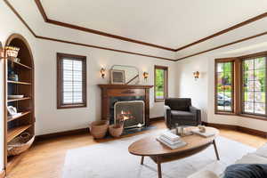 Living room featuring a wood-surround fireplace with a black stone hearth, recessed built-in shelving, wood-finish flooring, and a bay window with wood trim