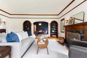 Living area featuring hardwood flooring, a substantial wood-mantel fireplace with a dark stone surround, and built-in arched bookcases with integrated lighting