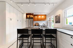 Modern kitchen featuring a central island with dark countertop, stainless steel refrigerator, white subway tile backsplash, and light wood cabinetry