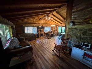 Spacious interior featuring wood-finish flooring, exposed wood beam ceilings, log walls, stone-faced fireplace, and multiple windows with blinds