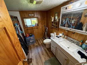 Bathroom featuring wood-finish wall paneling, a single vanity with a white countertop and integrated sink, a mirrored medicine cabinet, a window, and wood-finish flooring