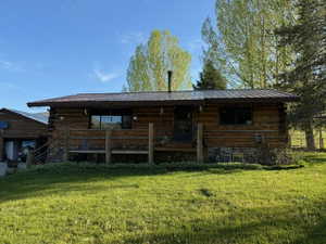 Log cabin exterior featuring a metal roof, a stone foundation, a covered porch with a wood railing, and a detached garage structure
