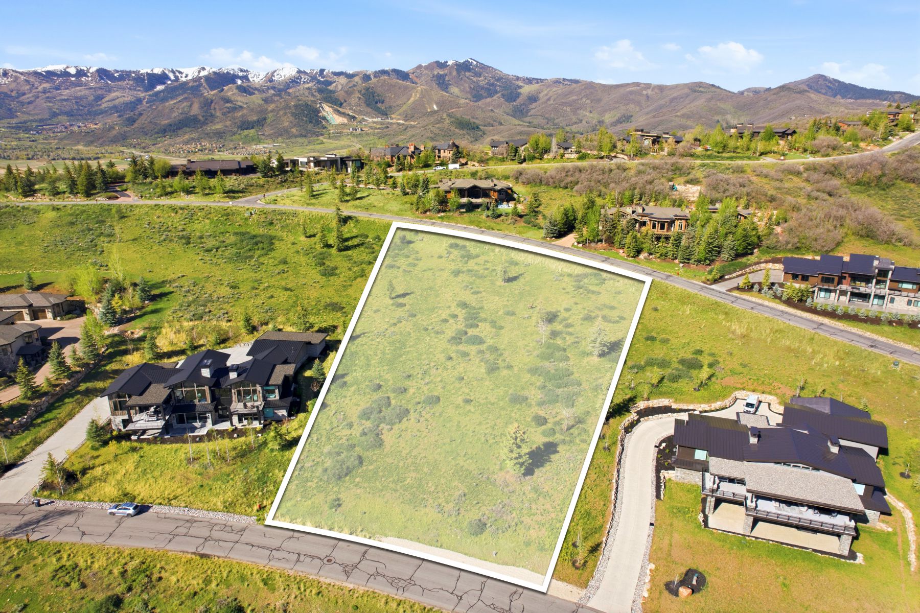 Expansive land parcel featuring natural ground cover, surrounded by mountain terrain, and bordered by paved roadways