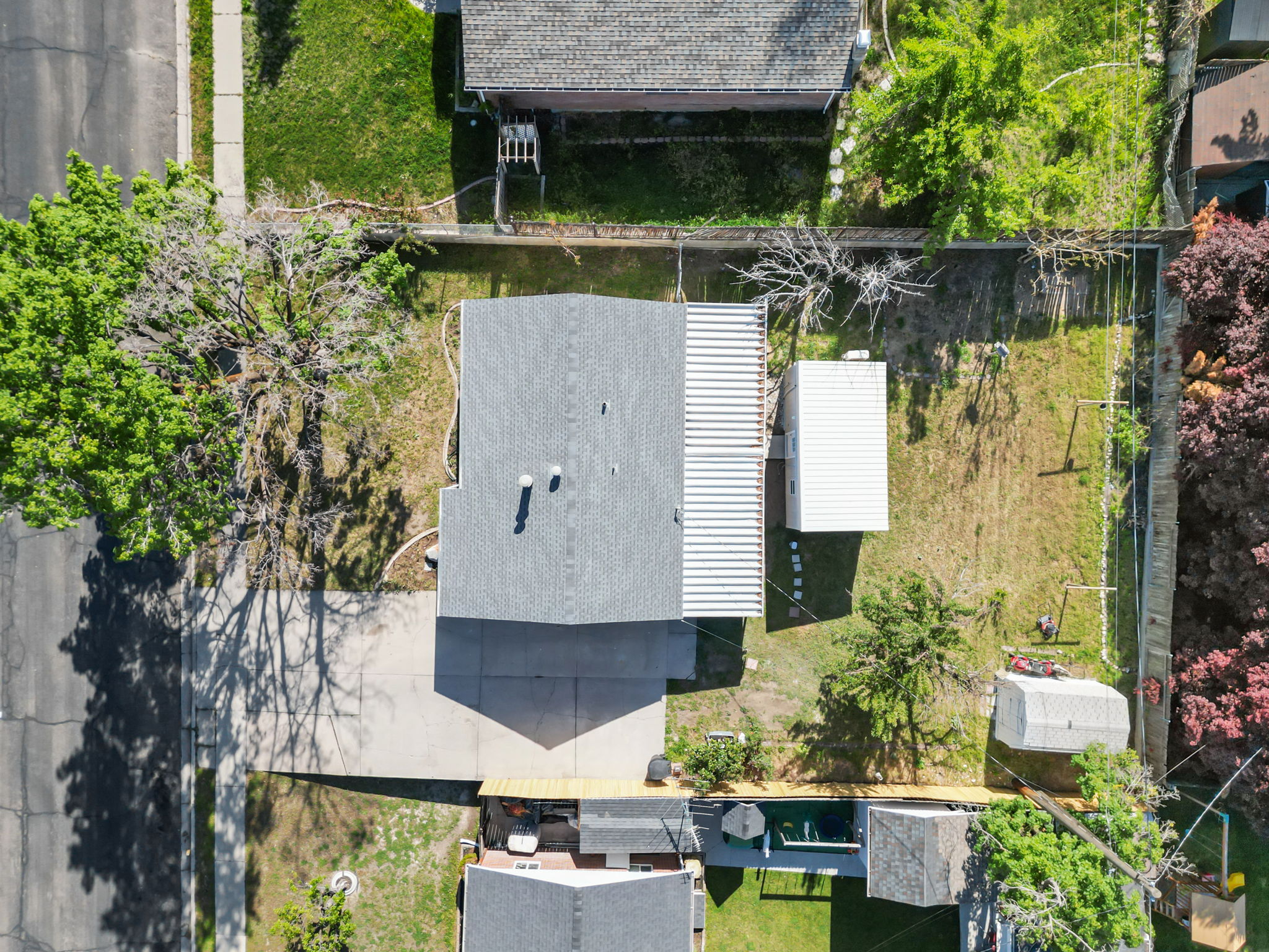 Aerial perspective showcasing a property with a gray shingled roof, an attached carport, and a detached white storage shed