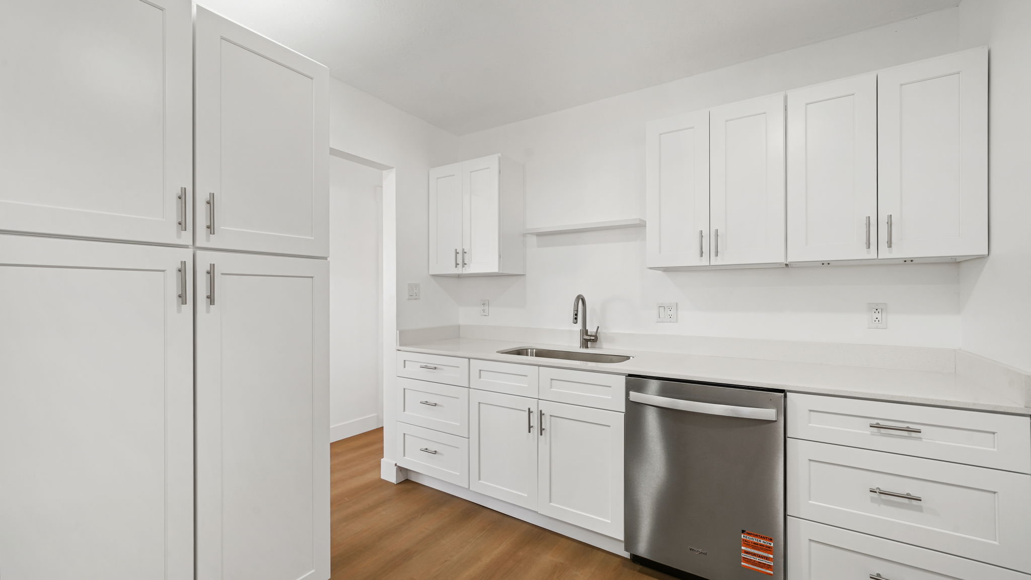Kitchen featuring white shaker-style cabinetry, light-toned countertops, and wood-finish flooring
