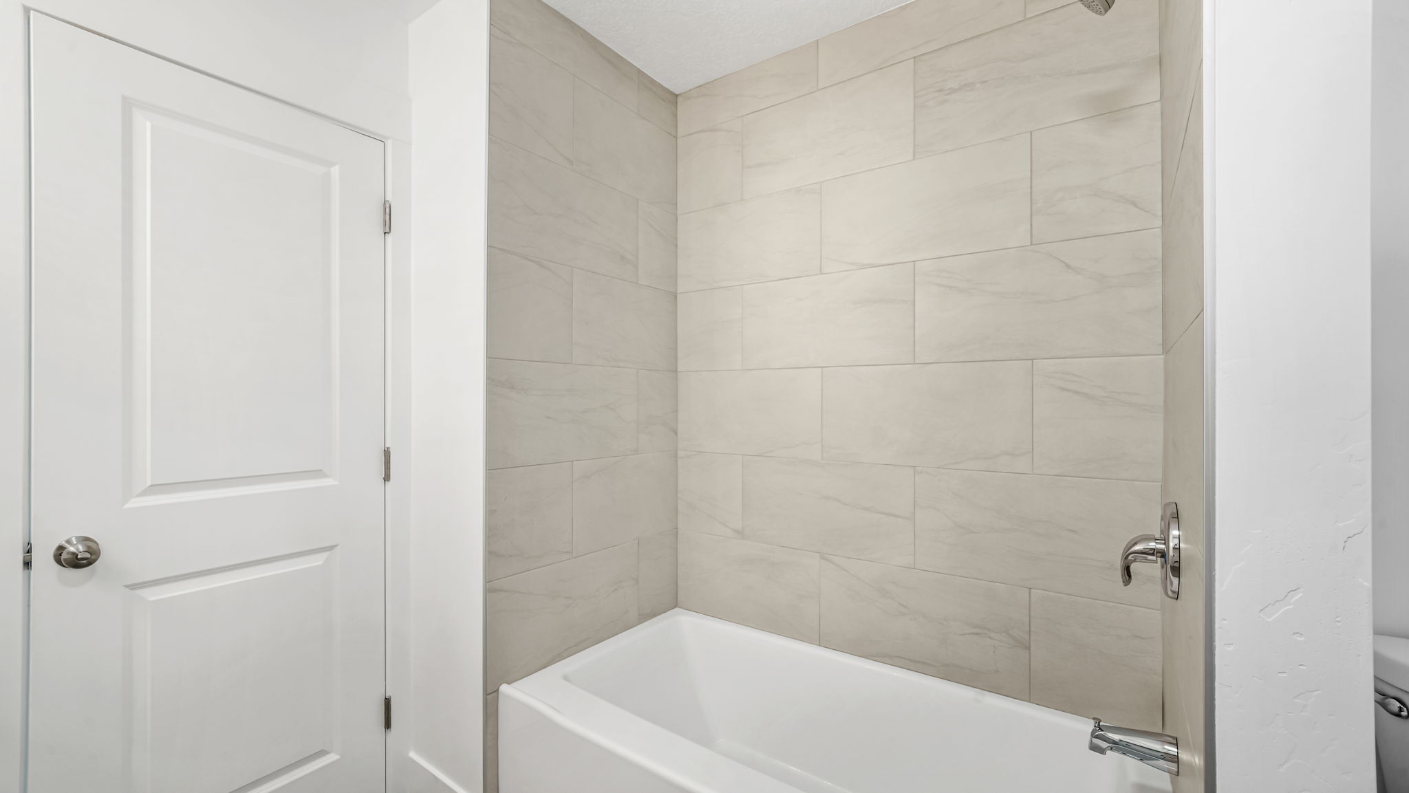 Bathtub with light-toned tiled surround and chrome fixtures