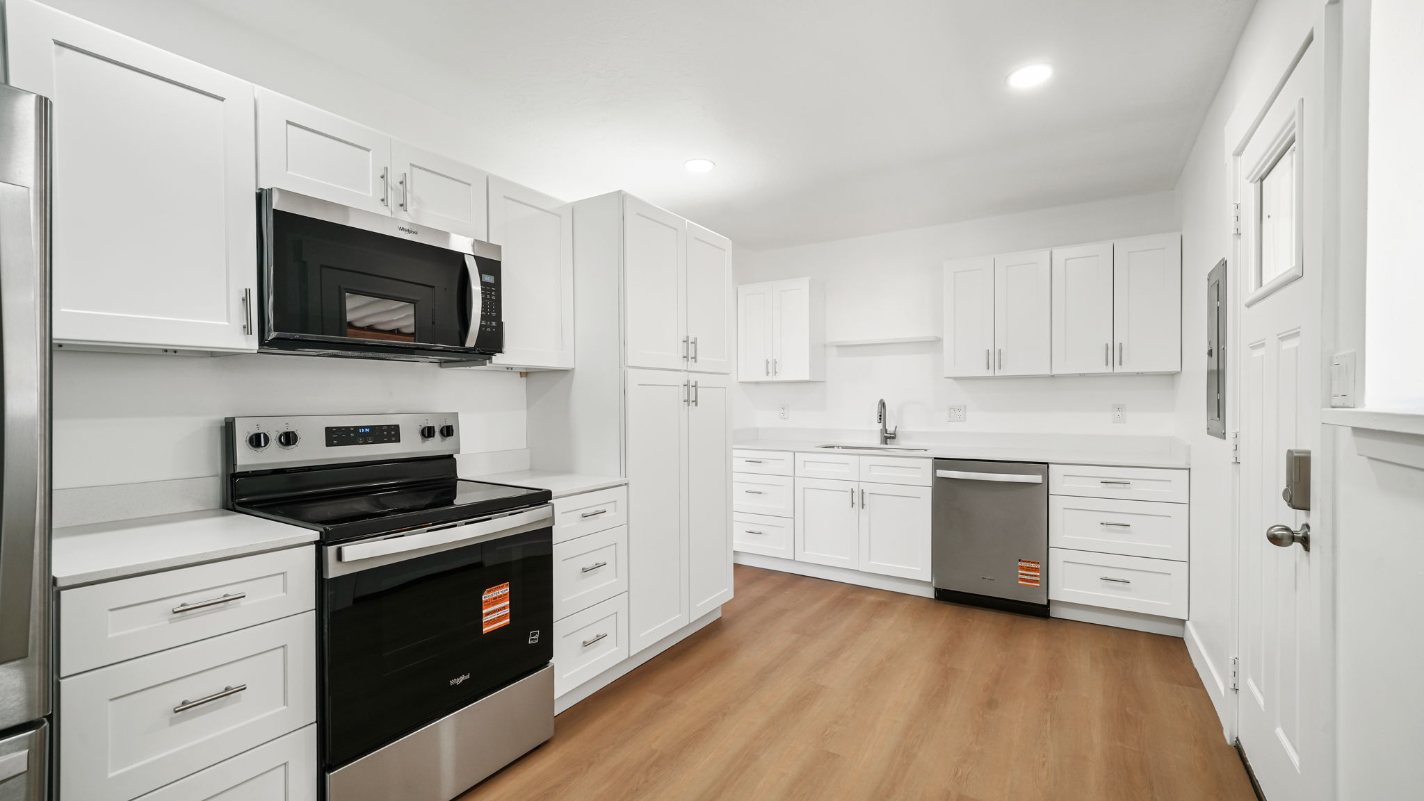 Modern kitchen featuring white shaker cabinetry, stainless steel appliances, light-toned countertops, wood-finish flooring, and recessed lighting