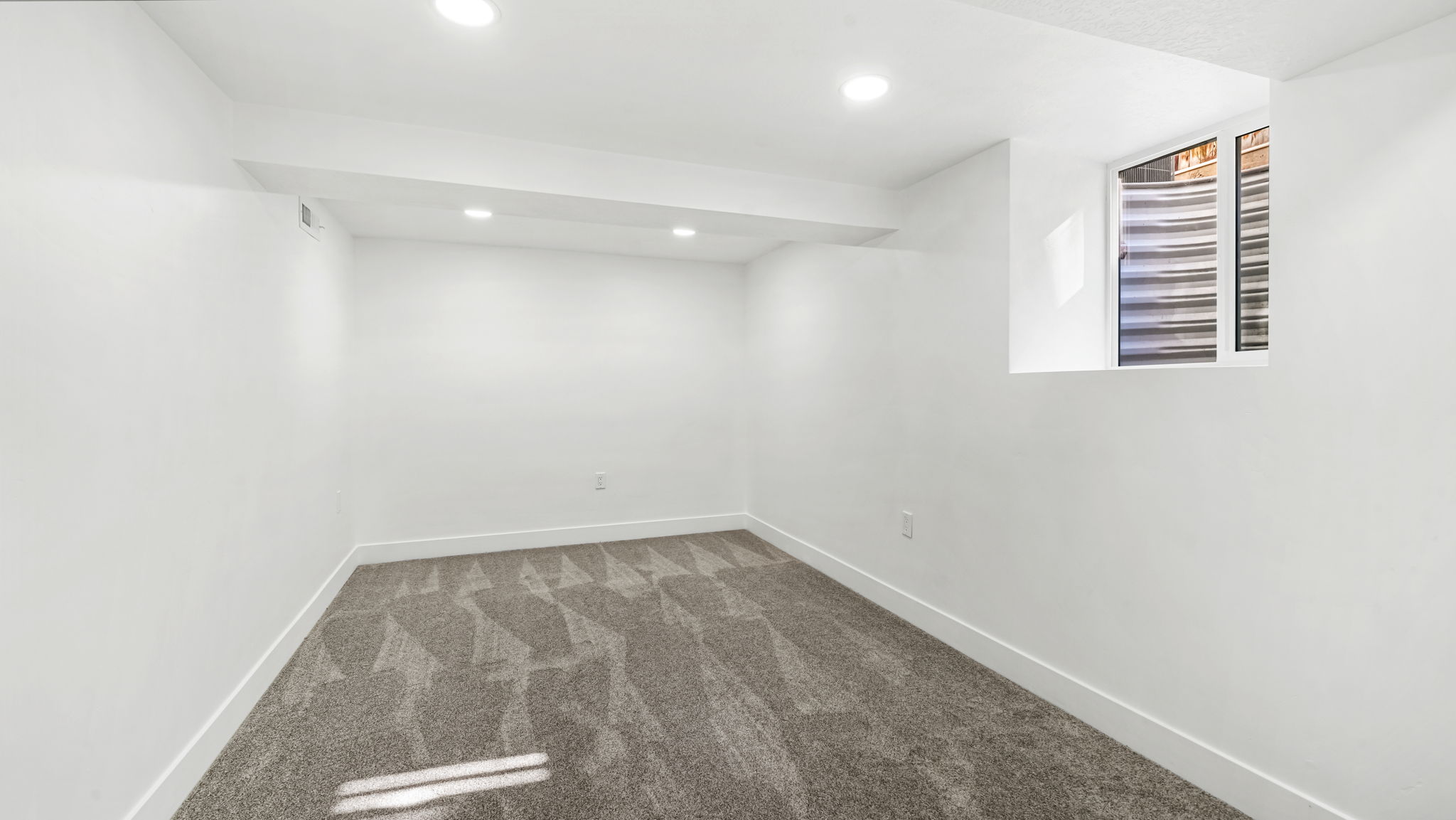 Neutral white walls with recessed ceiling lighting, a patterned grey carpet, and a high-set window