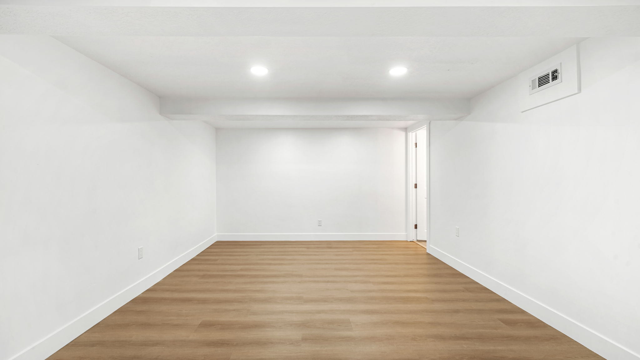 Spacious room featuring wood-finish flooring, recessed lighting, white walls, white baseboards, and a white ceiling with exposed ductwork