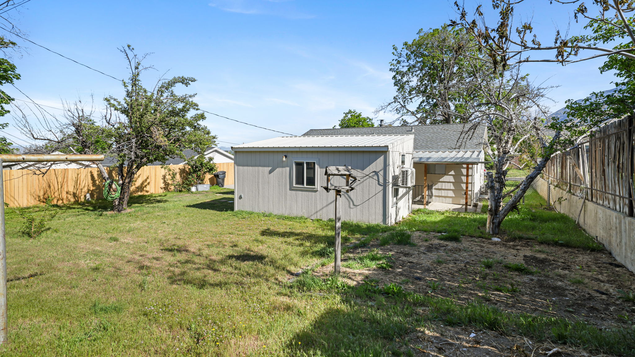 Spacious backyard featuring a detached outbuilding, mature trees, a wood privacy fence, and a concrete patio