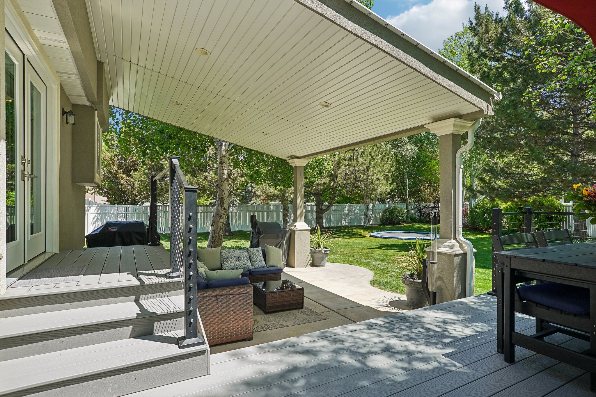 Expansive covered patio featuring a light grey composite deck, white painted support columns, and access to a manicured lawn