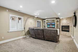 Entertainment space featuring a built-in media center with shelving, a fireplace with stone surround, recessed lighting, and patterned carpeting